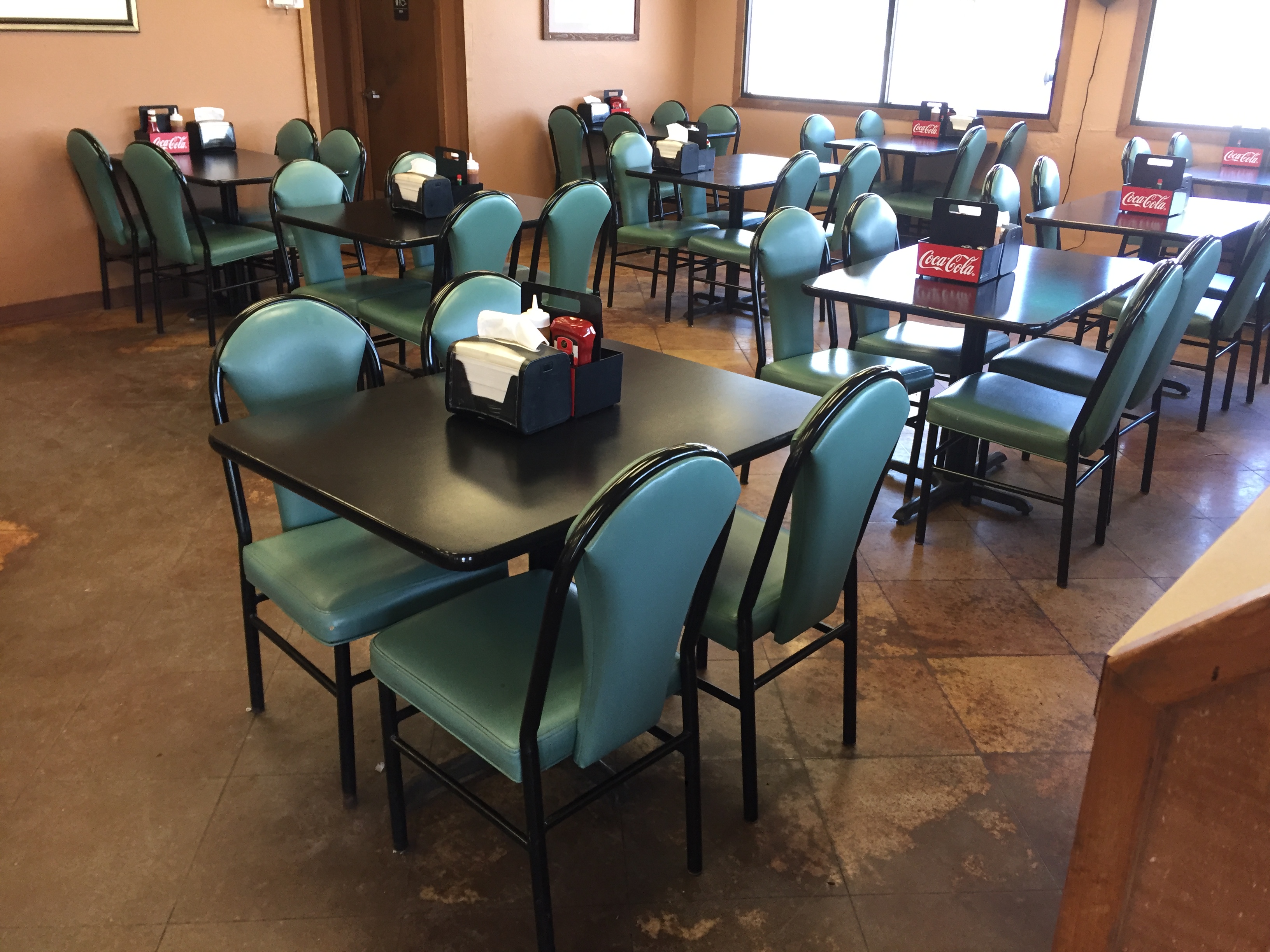 Inside The Sticks BBQ dining room — teal padded chairs, black square tables with Coca-Cola caddies, warm orange walls, Brownwood TX
