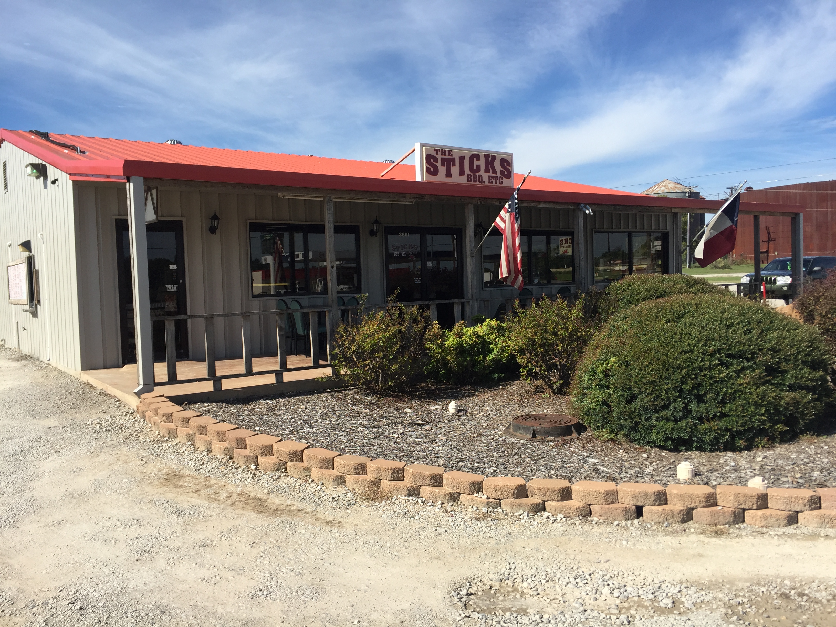 The Sticks BBQ restaurant exterior — 3501 US-377, Brownwood, TX, red metal roof with American and Texas flags